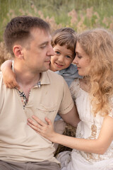 Fototapeta premium Happy family, cuddling in the field, mom and dad love their son, baby with golden hair, blonde woman, beautiful people, games with parents, bright children