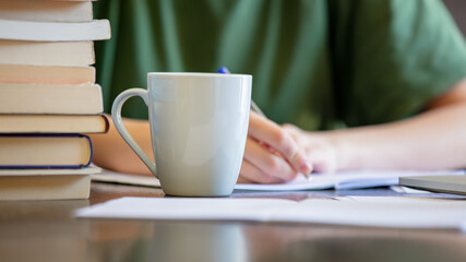 Woman is writing something in to notebook near coffee cup