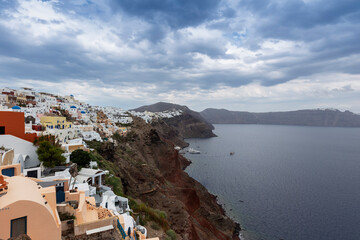 Santorini - Oia, view from the cliff to the caldera. On the left, a stone path that leads to white Greek houses that stand on a cliff. In the background the sea and the island.