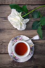 White rose and a cup of tea on a wooden background