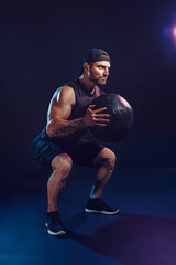 Aggressive bearded muscular sportsman is working out with a medicine ball isolated on dark studio...