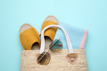 Wicker bag with beach objects on light blue background, flat lay