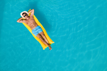 Happy man with inflatable mattress in swimming pool, top view and space for text. Summer vacation