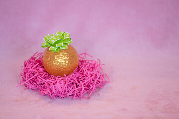 Festive Easter decorations and pink background. Chocolate sphere wrapped in gold with a green ribbon.