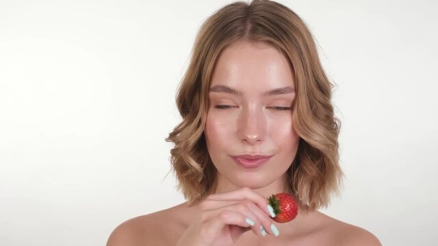 Beautiful tender young girl in a white home bathrobe with clean fresh skin posing in front of the camera with a Strawberry in her hands. Beauty face. Skin care.