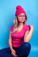 Fototapeta premium young pretty teenage modern hipster girl posing emotional happy on blue background, wearing pink hat and glasses, lifestyle people concept