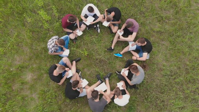Teamwork concept. A group of high school students sit on the grass in a circle. Drone view.