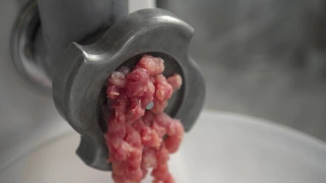Electric mincer machine closeup. Filling comes out through meat grinder sieve. Grinder with fresh chopped meat. Process of raw meat grinding in kitchen with mincing machine. Preparation of minced beef