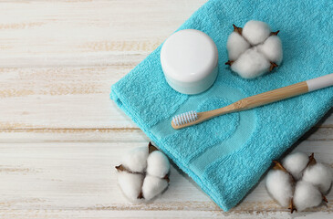 Obraz na płótnie Canvas A wooden toothbrush , a jar of tooth powder, and cotton flowers lie on a folded blue soft towel on a wooden white background. Oral hygiene. Selective focus. Zero waste. Top view