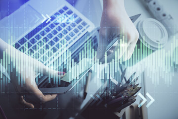 Double exposure of businesswoman hands typing on computer and financial graph hologram drawing....