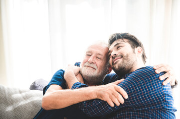 An adult hipster son and senior father talking on sofa at home, family concept