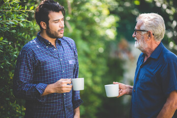 An adult hipster son and senior father talking at home, morning nature scene in the home garden...