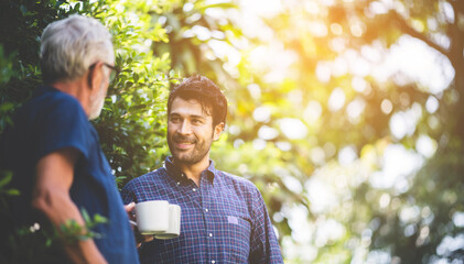 senior father and adult son with coffee cup talking in the garden at home, relax morning time