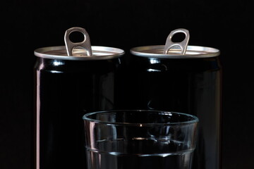 transparent glass cup and two aluminum cans arranged on a black background.