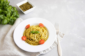A plate with traditional Italian pasta pesto with cherry tomatoes, next to a gravy boat with basil sauce.