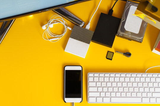 table with yellow background, several different hds, phone, screen, keyboard. Top view.  