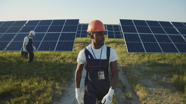 Afro-american Young Worker Walking On Solar Panel Field. Ecological Installation. Industrial Evolution. Green Energy Jobs. Electricity. Technology.