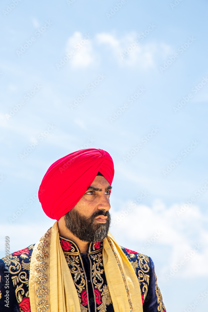 Wall mural Attractive male Sikh model in traditional wedding attire on beach beneath sunny blue skies - Wall murals