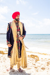Fototapeta premium Attractive male Sikh model in traditional wedding attire on beach beneath sunny blue skies