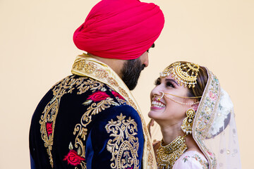 Sikh bride and groom wearing bright traditional clothing on clear sandy beach beneath sunny blue skies