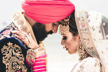 Sikh bride and groom wearing bright traditional clothing on clear sandy beach beneath sunny blue skies