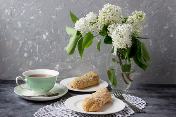 Cup of tea,  delicious eclairs with bouquet white lilac bouquet.