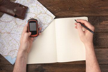 Travel planning concept. Hand writing in blank notepad with gps navigator, knife and map on wooden...