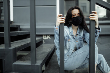 Fototapeta premium Sad teenager girl in medical mask behind bars. Schools are quarantined due to illness, epidemics. Coronavirus pandemic. Covid 19