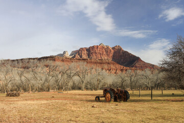 rusty vintage tractor sitting in dry field with red rock mountain