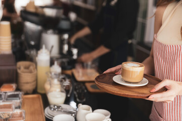 Young woman barista standing at coffee shop holding cup serving order fresh hot latte at coffee shop.