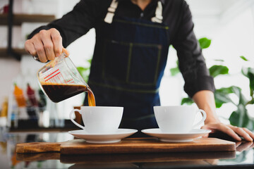 Barista pouring black coffee to white cup for service in coffee shop.