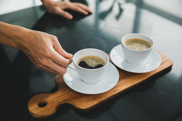 Two cup of black coffee on wooden tray with a hand of barista in the morning.