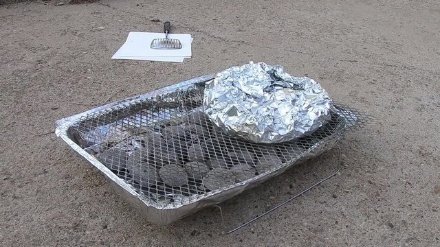 Potatos in aluminum tin foil on a throw away BBQ sitting in a driveway on a sunny day.
