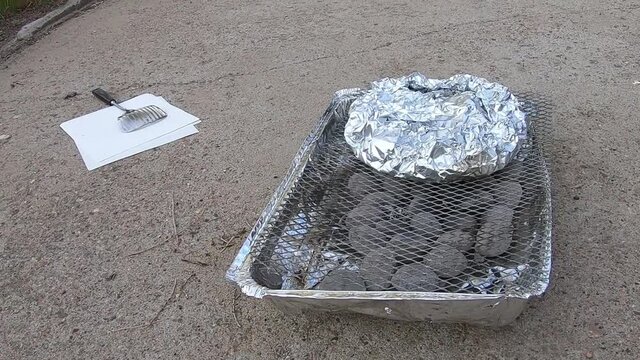 Potatos in aluminum tin foil on a throw away BBQ sitting in a driveway on a sunny day.