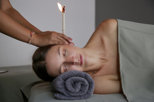 Woman receiving ear candle treatment at spa. Ear coning or thermal-auricular therapy. - Powered by Adobe
