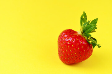 one large ripe red strawberry on a yellow background close up