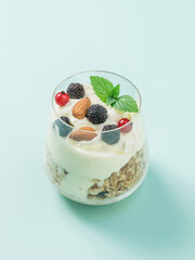 Glass with almonds, berries, granola and yogurt on a light blue background.