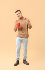 Handsome young man with cup of tea on color background