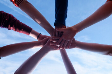 Unification in a group of people and the power of unity of the team. Partnership spirit concept. People hold hands together and boys and girls, adults and young on the sky background.