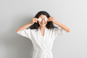 Beautiful young woman with cotton pads on light background