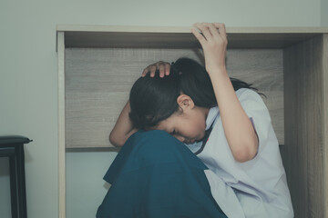 Asian young girl in a school uniform hides under the desk when an earthquake occurs with concept
