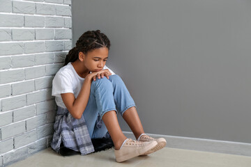 Sad African-American girl sitting near grey wall. Stop racism