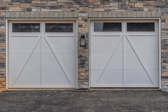 Two Single White Garage Doors With Raised Panel And Windows On A Facade Covered With Manufactured Stone Veneer