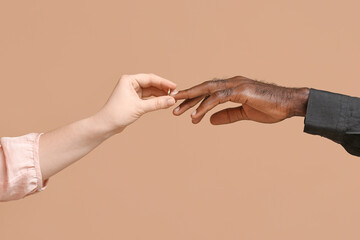 Caucasian woman putting wedding ring on finger of African-American man against color background....
