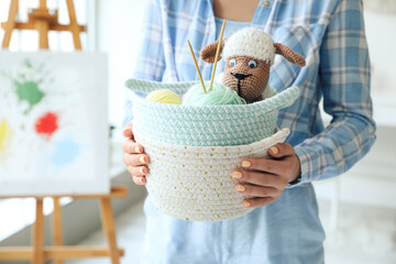 Woman holding wicker baskets with toys and knitting yarn in room