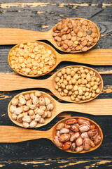 Spoons with raw legumes on dark wooden background