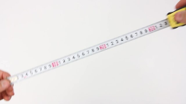 human hands pull the measuring tape out of tape measure and measure the dimensions, length width height and diagonal, then removes it, close up view on white background