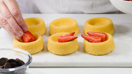 Biscuit cakes with fresh berries, chocolate, and whipped heavy cream. Woman preparing dessert, mini biscuit cups with strawberries and blueberries,  close up on white background