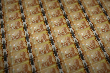 100 Canadian dollars bills printed in illegal money production conveyor. Collage of many fake...