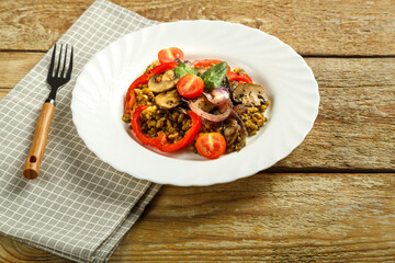 On a wooden table is a white plate of boiled mung bean with mushrooms and vegetables on a napkin and a fork.